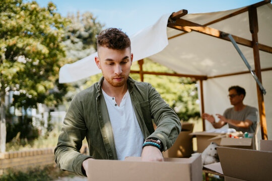 Young male volunteer searching in cardboard box during charity drive at community center