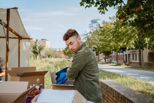 Side view of young male volunteer packing clothes in cardboard boxes while working during charity drive at community cen