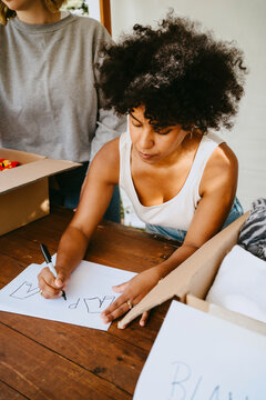 Young female volunteer with curly hair making name tags while leaning on table at community center