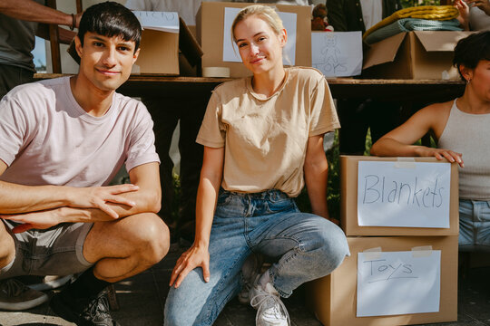 Portrait of smiling male and female volunteers crouching by donation boxes at community center