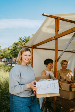 Portrait of happy volunteer holding sweater box during charity drive at community center
