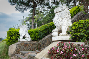 Obraz premium Lion statues. Two marble lions sit on a staircase on pedestals in front of the public park in Da Lat Vietnam