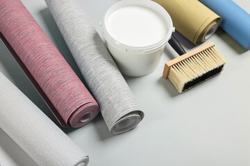 Wallpaper rolls, brush and bucket of glue on light grey background