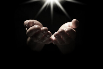 Christian woman holding hands under holy light in darkness, closeup. Prayer and belief