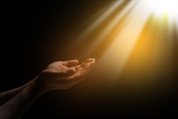 Christian man stretching hands towards holy light in darkness, closeup. Prayer and belief