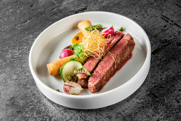 A gourmet plated meal featuring succulent steak, colorful vegetables, and garnish on a white plate. The top view showcases the juicy steak alongside vibrant vegetables, all beautifully presented