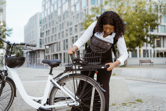 Businesswoman removing battery from electric cycle in city
