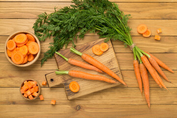 Bunch of fresh carrots with sliced ones on wooden background, top view