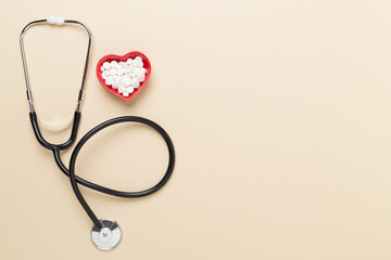 Stethoscope with heart medicines on color background, top view