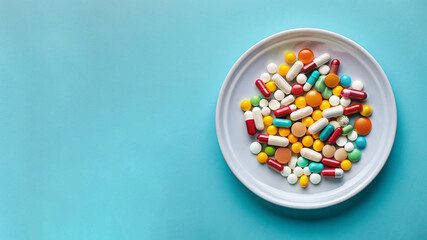 top view of a white plate with multicolored tablets and pills on a blue studio background with space for text