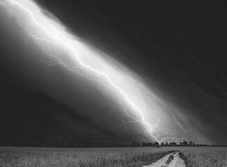 Dramatic Rain Sky With Rain Clouds On Horizon Above Rural Landscape Camola Colza Rapeseed Field. Country Road. Agricultural And Weather Forecast Concept. black and white