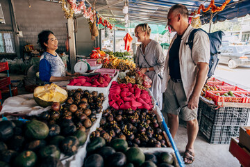 Male and female senior tourists buying fruits from vendor at market stall