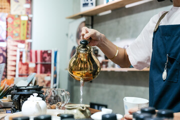 A tea master in a Glodok teahouse, Jakarta’s Chinatown, elegantly pours tea from a golden teapot, creating a warm and authentic atmosphere rich in Chinese tea culture and tradition.
