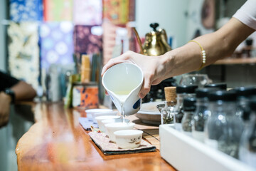 A tea master in a Glodok teahouse, Jakarta’s Chinatown, elegantly pours tea from a golden teapot, creating a warm and authentic atmosphere rich in Chinese tea culture and tradition.
