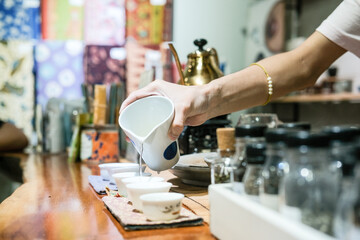 A tea master in a Glodok teahouse, Jakarta’s Chinatown, elegantly pours tea from a golden teapot, creating a warm and authentic atmosphere rich in Chinese tea culture and tradition.
