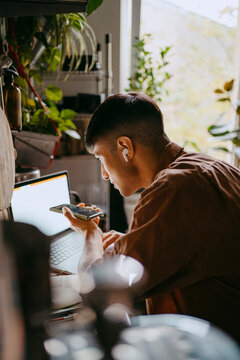 Male freelancer talking on speaker phone while using laptop in kitchen at home office
