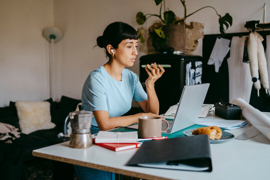 Female business professional talking on speaker phone and using laptop at desk in home office