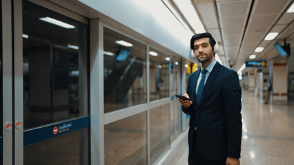 Project manager wearing headphone at train station while holding mobile phone for choosing song....