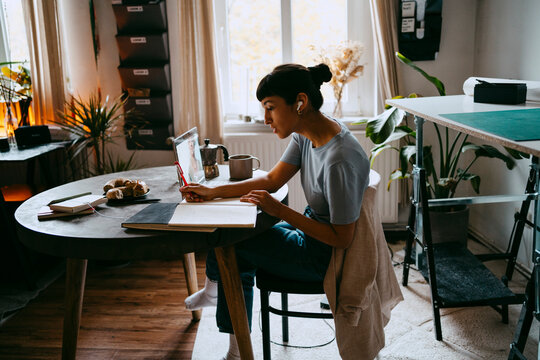 Side view of female business professional planning strategy with colleague on video call through laptop at home office