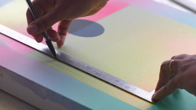 A diverse biracial female artist, draws straight lines with a pencil and a right angle ruler onto a painted artist canvas. The canvas has soft pastel gradients and a black circle sun or moon