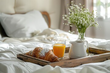 breakfast on the bed in hotel room, wooden tray with coffee and croissant glass of orange juice vase with flowers white milk jug
