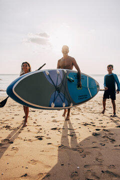 Man carrying surfboard while walking with son and daughter on sand at beach against sky