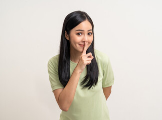 Happy beautiful young asian woman whispering some secret gossip. Excited pretty latin girl index finger on mouth standing pose on isolated white background.