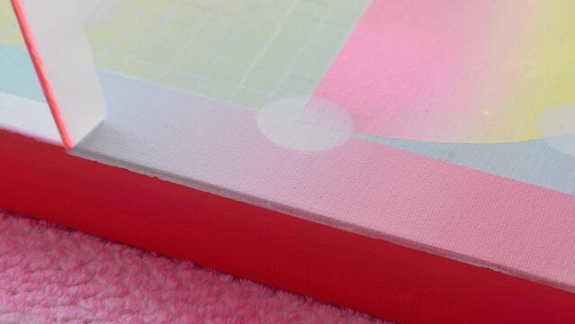 An artist pulls masking tape, to reveal a crisp hard edge gradient painted artist canvas. The canvas edge is bright neon orange.