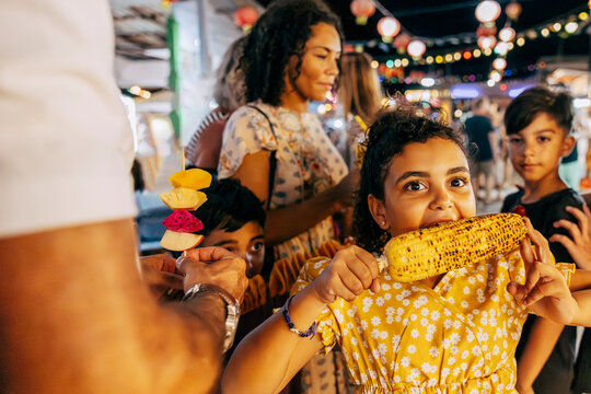 Girl eating grilled corn with family at food market on vacation