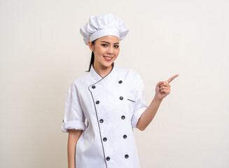 Smiling Young beautiful asian woman chef in uniform pointing finger to copy space isolated background. Cooking woman Occupation chef or baker People in kitchen restaurant and hotel.