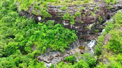 Aerial view: Majestic waterfall cascading from lush tropical cliff, captured by a drone, showcasing nature's raw beauty. Soi Sawan Waterfall, Pha Taem National Park, Ubon Ratchathani, Thailand.
