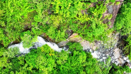 Aerial view of cascading waterfall, lush tropical forest, and towering cliff, captured by a drone. Serene natural beauty. Soi Sawan Waterfall, Pha Taem National Park, Ubon Ratchathani, Thailand.
