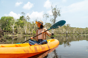 Holiday travel activities. Happy asian woman rowing a canoe or kayak in mangrove forests. Young...