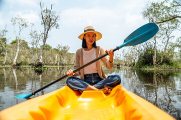 Holiday travel activities. Happy asian woman rowing a canoe or kayak in mangrove forests. Young...