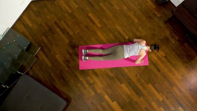 Overhead view of a person performing burpees on a pink mat, wooden floor background, indoor fitness concept