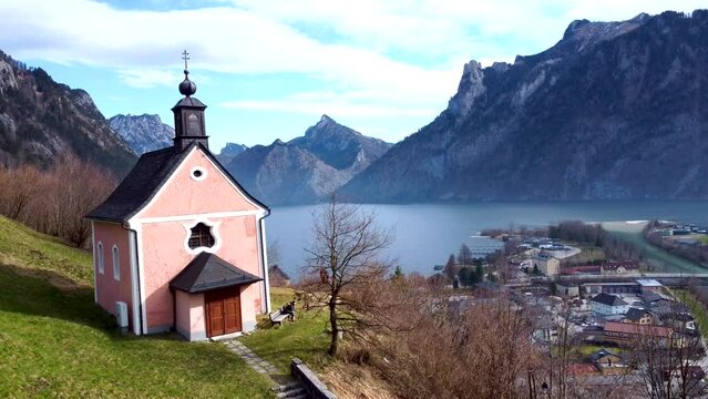 Drone shot pans down on a pink chapel on Kalvarienberg in Ebensee, with Traunsee lake in the background, peaceful and serene, Upper Austria