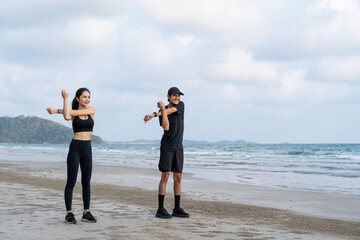 Asian Couple stretching arms and legs before running outdoors sea sand beach. Sporty people warm up...