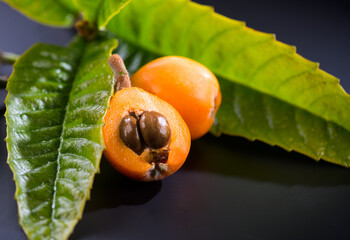 Loquat fruit or Japanese medlars, Nispero, Eriobotrya japonica with leaves fresh ripe bio vegetarian food, medlar berries. Close up. On black background