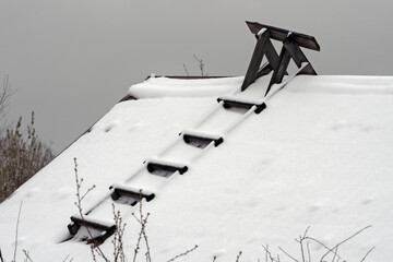 The snow-covered slope of the roof of an old village house on a spring day