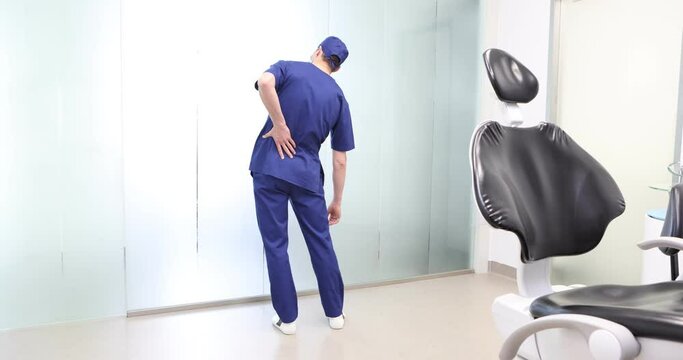 Standing dentist, dealing with lower back pain.Symptoms and self help exercises, stretching.  Back view.