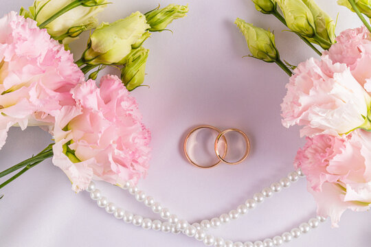 Two gold classic wedding rings on a white satin background with fresh pink austoma flowers. A copy space. postcard. invitation. cover.