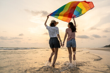 Young couple asian lesbian with pride movement LGBT holding rainbow flag for freedom. Demonstrate...