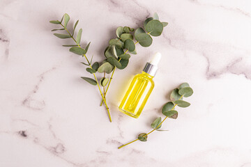 Herbal extract serum or eucalyptus oil in a glass bottle with a dropper on a white marble background with eucalyptus sprigs. Natural cosmetics.