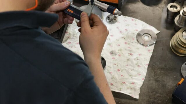 Worker measuring metal part with micrometer in workshop, close-up, industrial setting