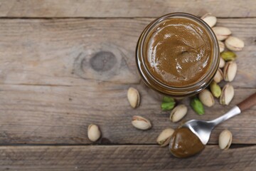 Tasty pistachio nut paste in jar and spoon on wooden table, flat lay. Space for text