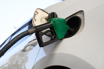 White car refueling at gas station with green fuel nozzle.