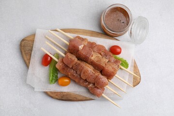 Wooden skewers with cut raw marinated meat on light grey table, flat lay