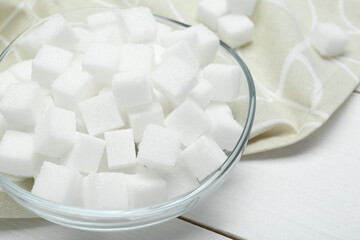 Many sugar cubes in glass bowl on white wooden table, closeup