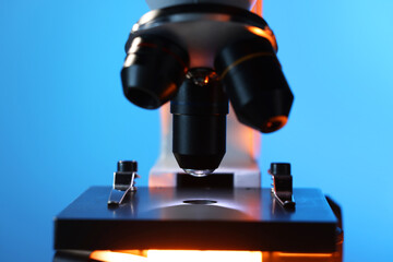 Microscope with glass slide on blue background, closeup
