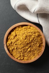 Dry curry powder in bowl on dark textured table, top view